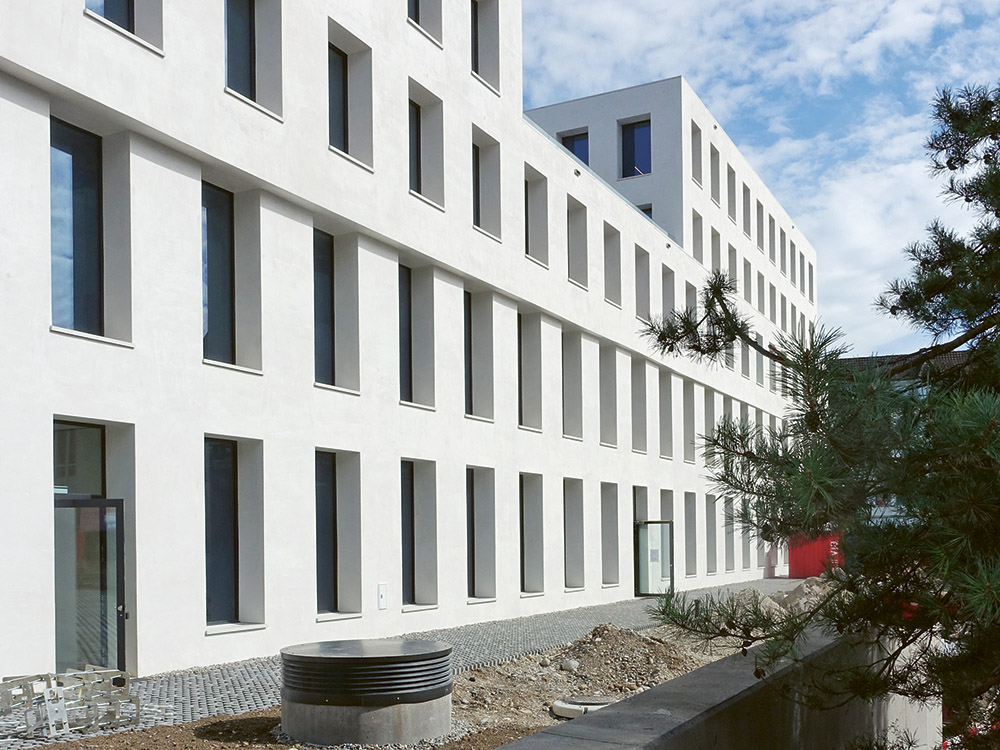 Versätze in der Fassade gliedern neben den Einkerbungen die regelmässige Fassade. Die Lochfenster sind nach bauphysikalischen Grundsätzen dimensioniert.